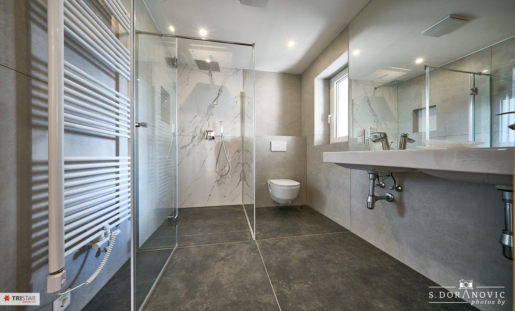 Stilvolles Badezimmer mit großer begehbarer Dusche, beheiztem Handtuchhalter und modernen Fliesen.