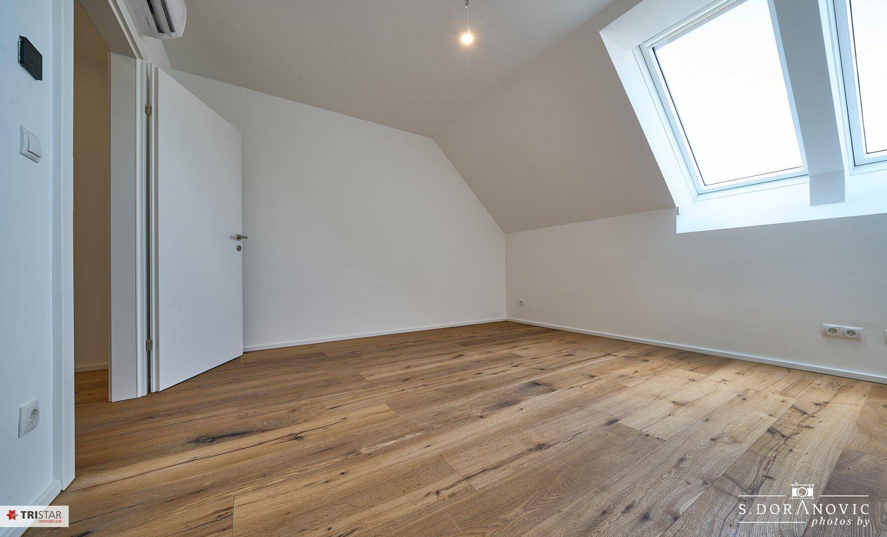Helles Dachzimmer mit Holzboden und Oberlicht, bietet eine gemütliche Wohnatmosphäre.
