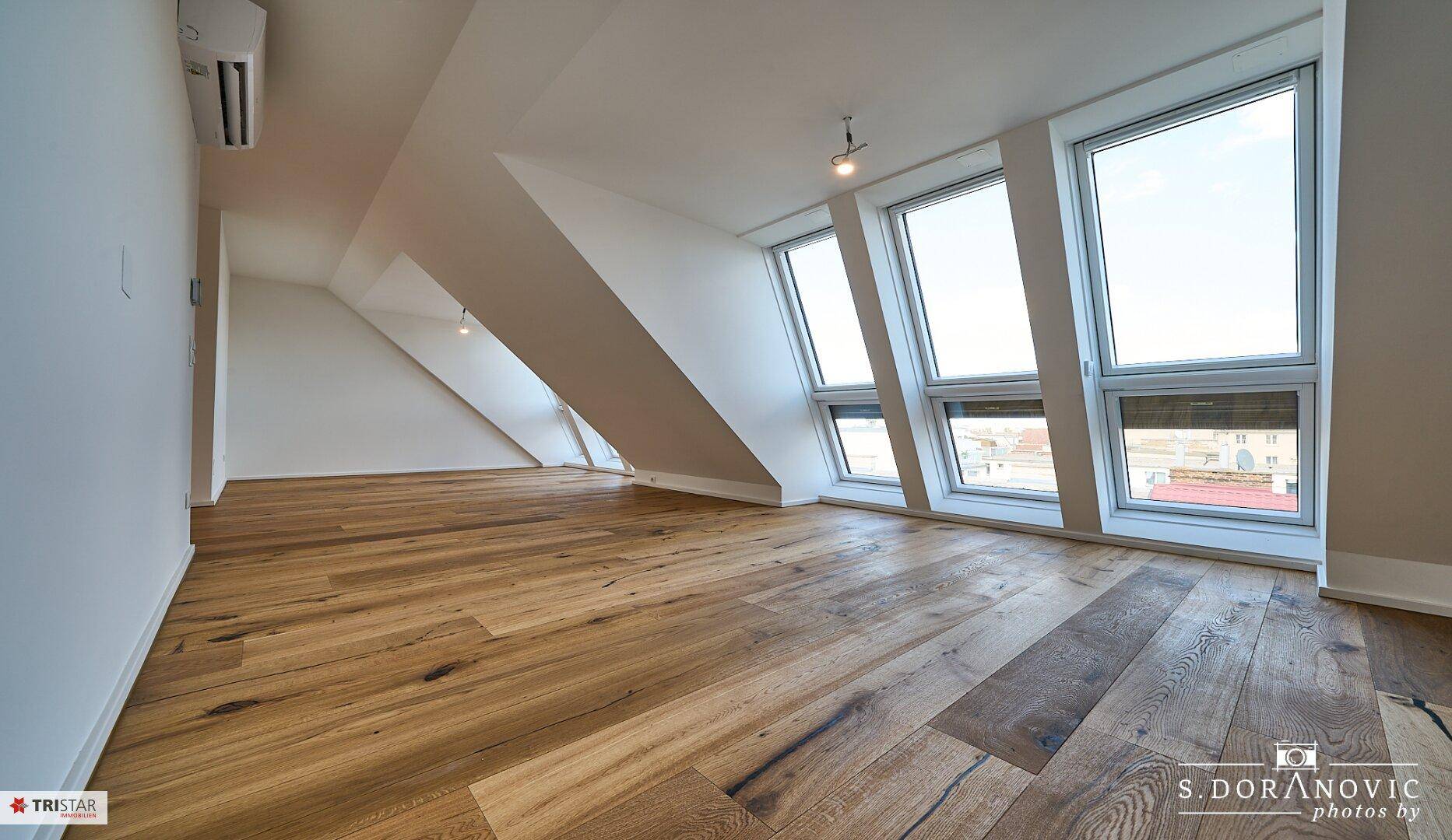 Heller Dachgeschossraum mit schrägen Wänden, Holzboden und modernen Fenstern, bietet viel Tageslicht.