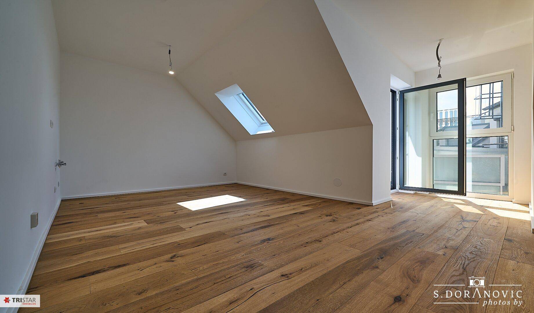 Heller Dachgeschossraum mit Holzboden und großem Schiebefenster zum Außenbereich.