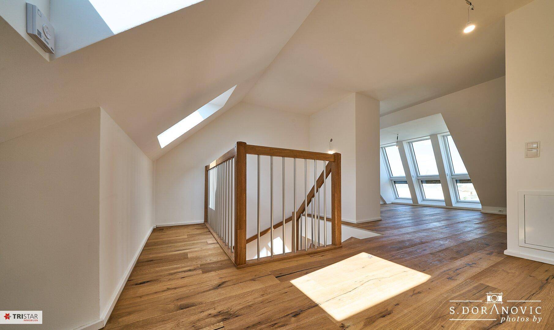 Heller Flurbereich im Dachgeschoss mit Holztreppe, Holzboden und Oberlichtern, verbindet die Ebenen.