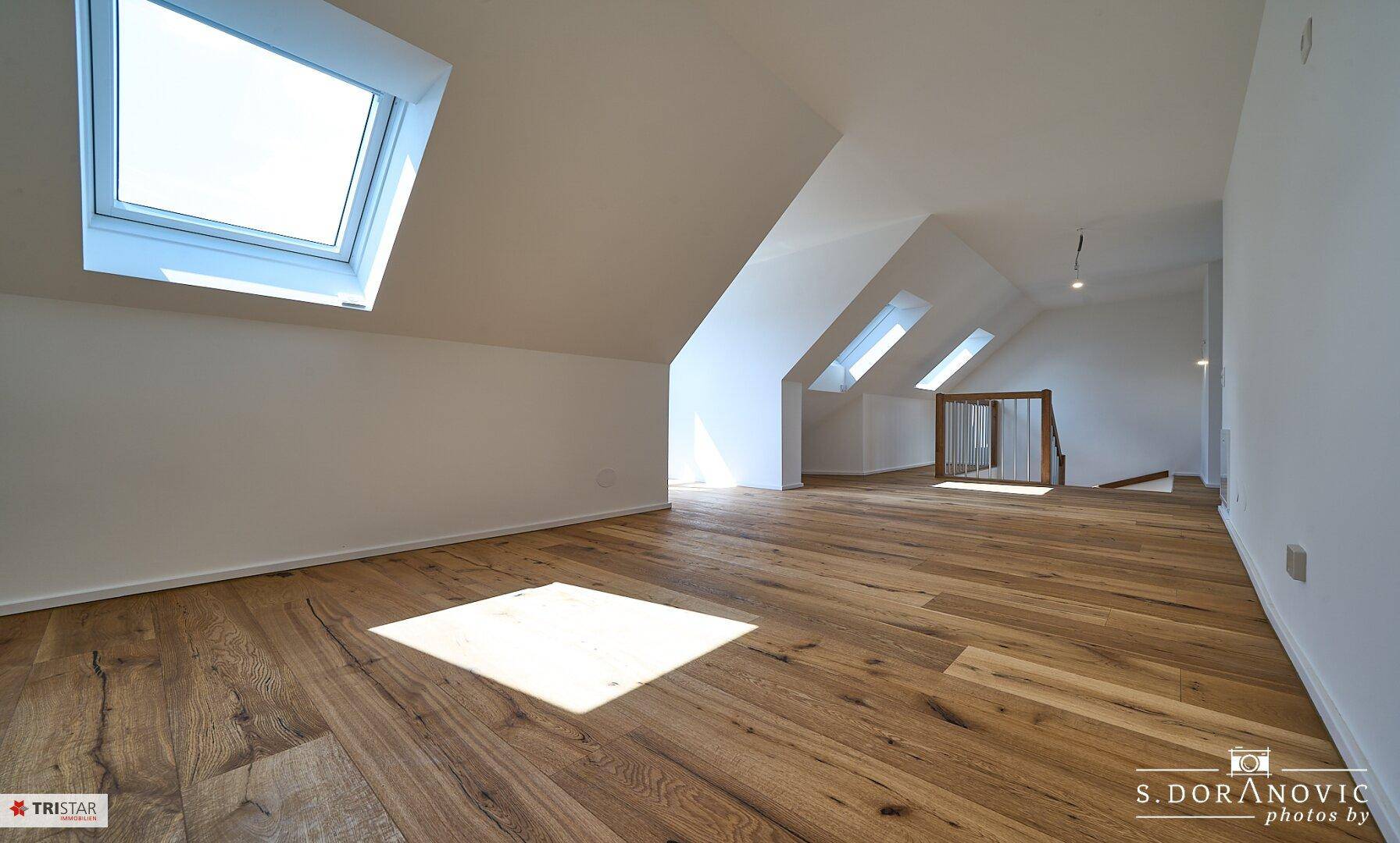 Heller Dachgeschossraum mit Holzboden und mehreren Oberlichtern, schafft eine freundliche Atmosphäre.