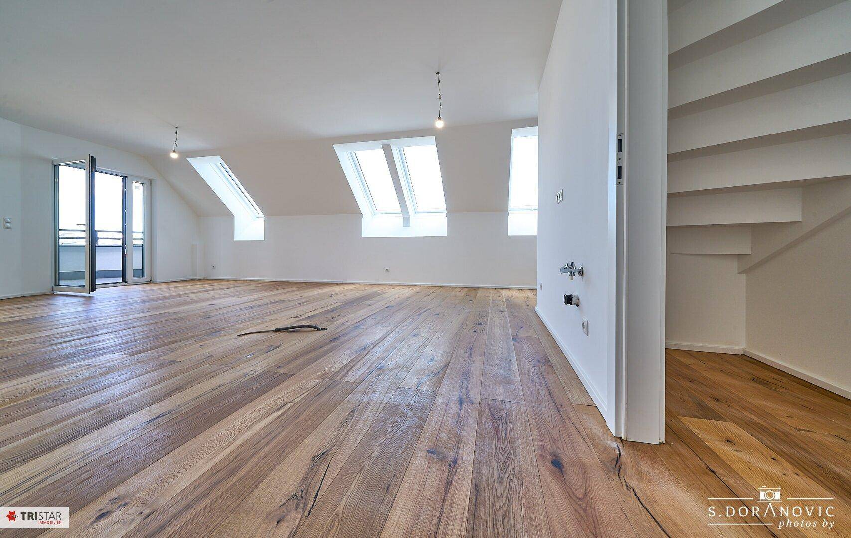 Geräumiger Wohnbereich im Dachgeschoss mit Holzboden, Dachfenstern und Zugang zum Balkon.