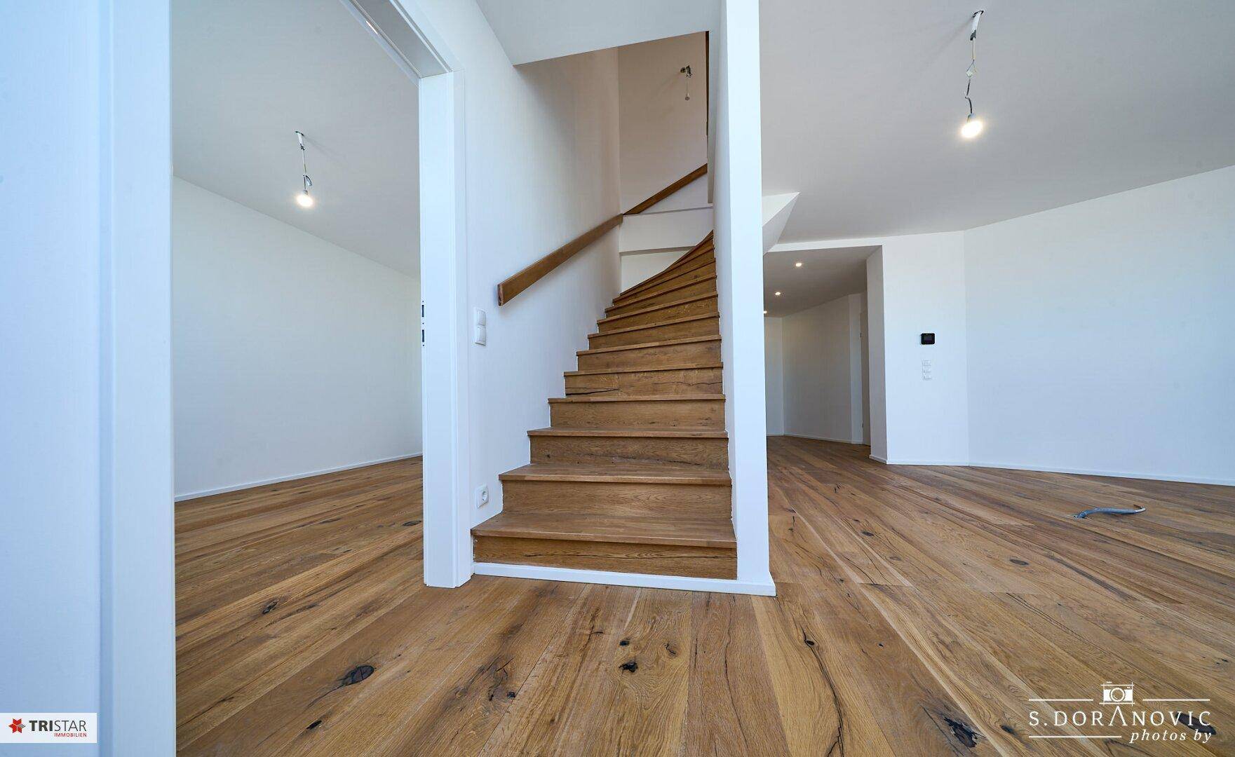 Heller Treppenbereich mit Holzstufen und weiß gestrichenen Wänden, verbindet die Ebenen der Wohnung.