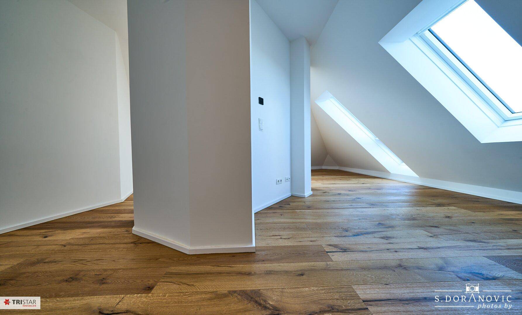 Heller Dachgeschossraum mit Holzboden und schrägen Wänden, bietet viel Potenzial für individuelle Gestaltung.