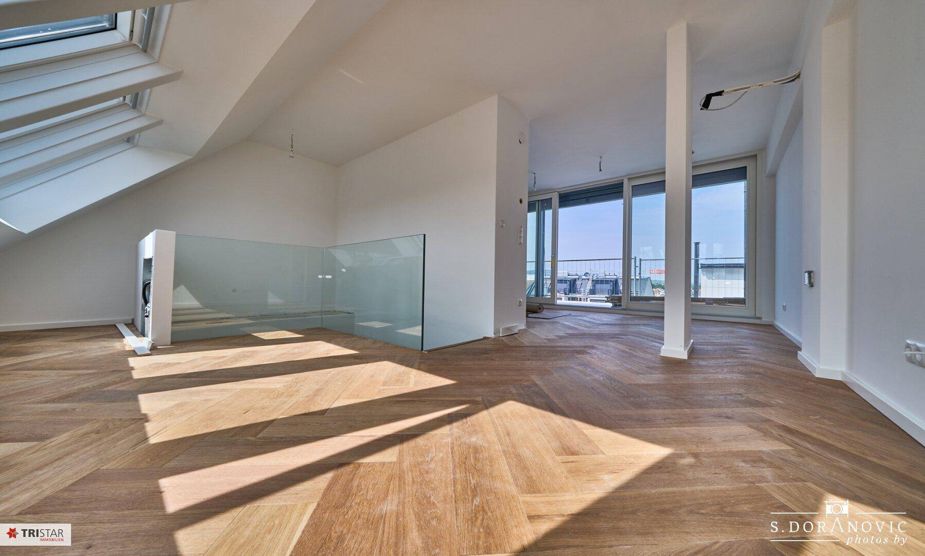 Heller Wohnbereich im Dachgeschoss mit modernem Fischgrätparkett, Dachfenster und Zugang zur Terrasse.