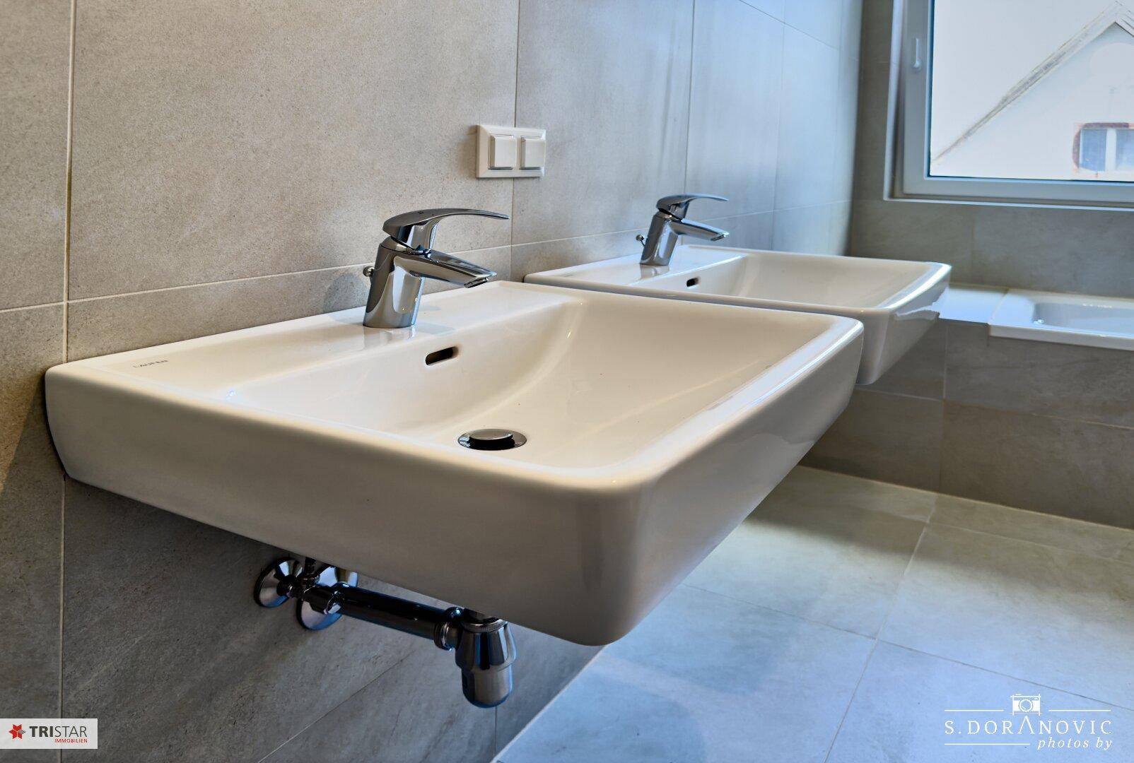 Nahaufnahme der modernen Doppelwaschbecken im hell gefliesten Badezimmer.