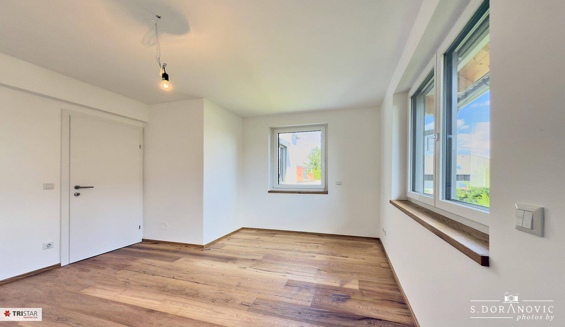 Helles Zimmer mit Eichenparkettboden und mehreren Fenstern, ideal als Schlaf- oder Wohnzimmer.