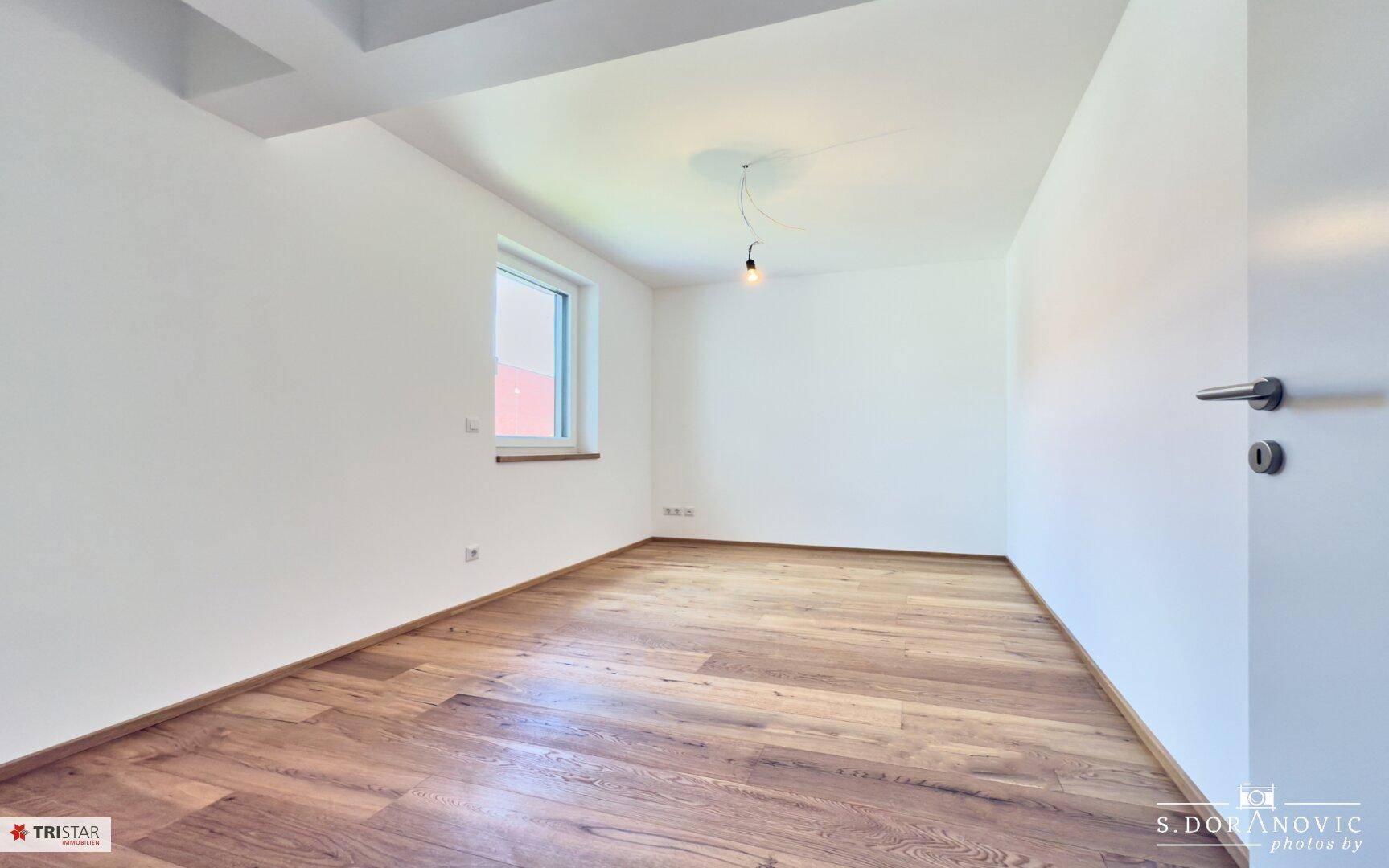 Geräumiges, helles Zimmer mit Holzboden und einem Fenster, bereit zur Einrichtung.