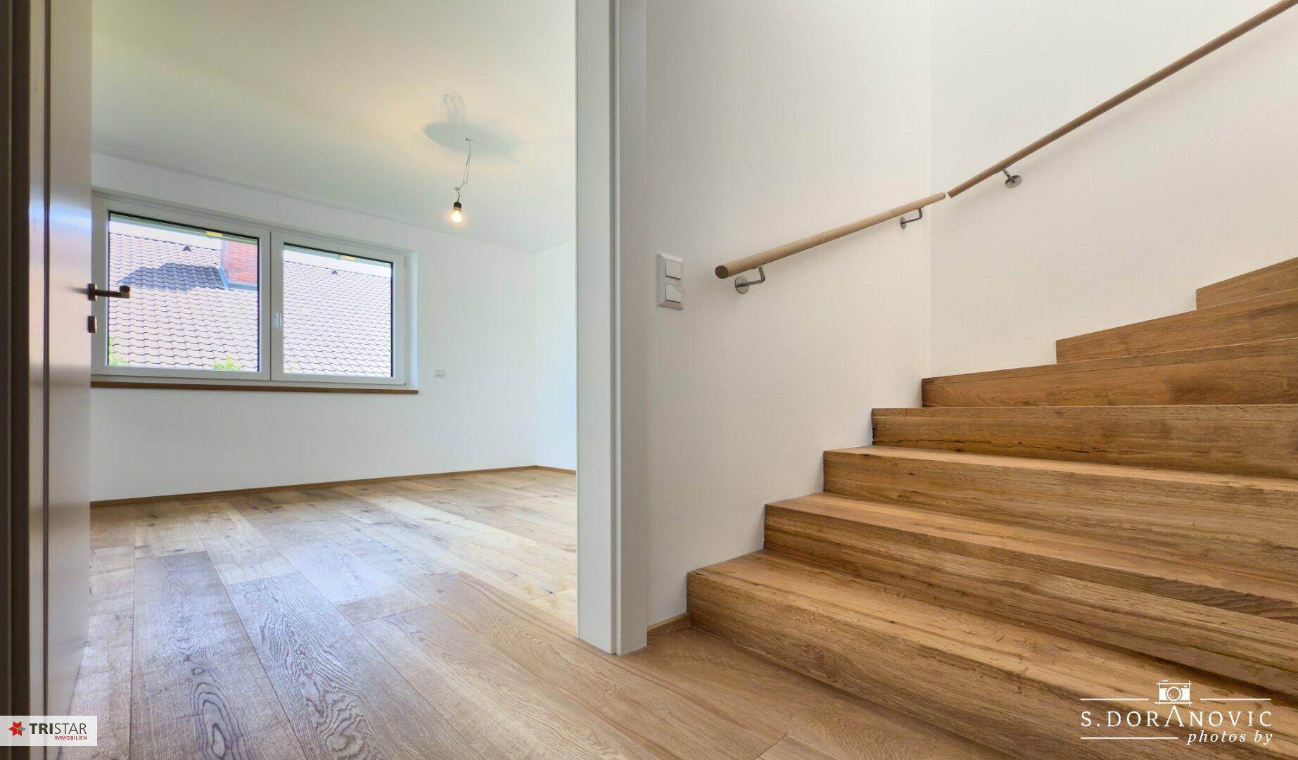 Heller Flur mit Holztreppe und Zugang zu einem weiteren Zimmer mit Holzboden.