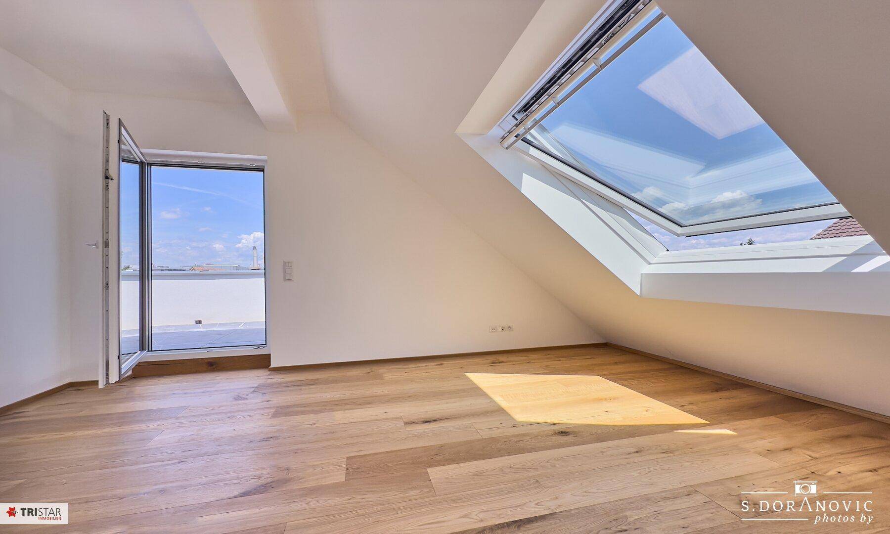 Lichtdurchflutetes Zimmer mit Holzboden, großem Dachfenster und direktem Zugang zur Terrasse.