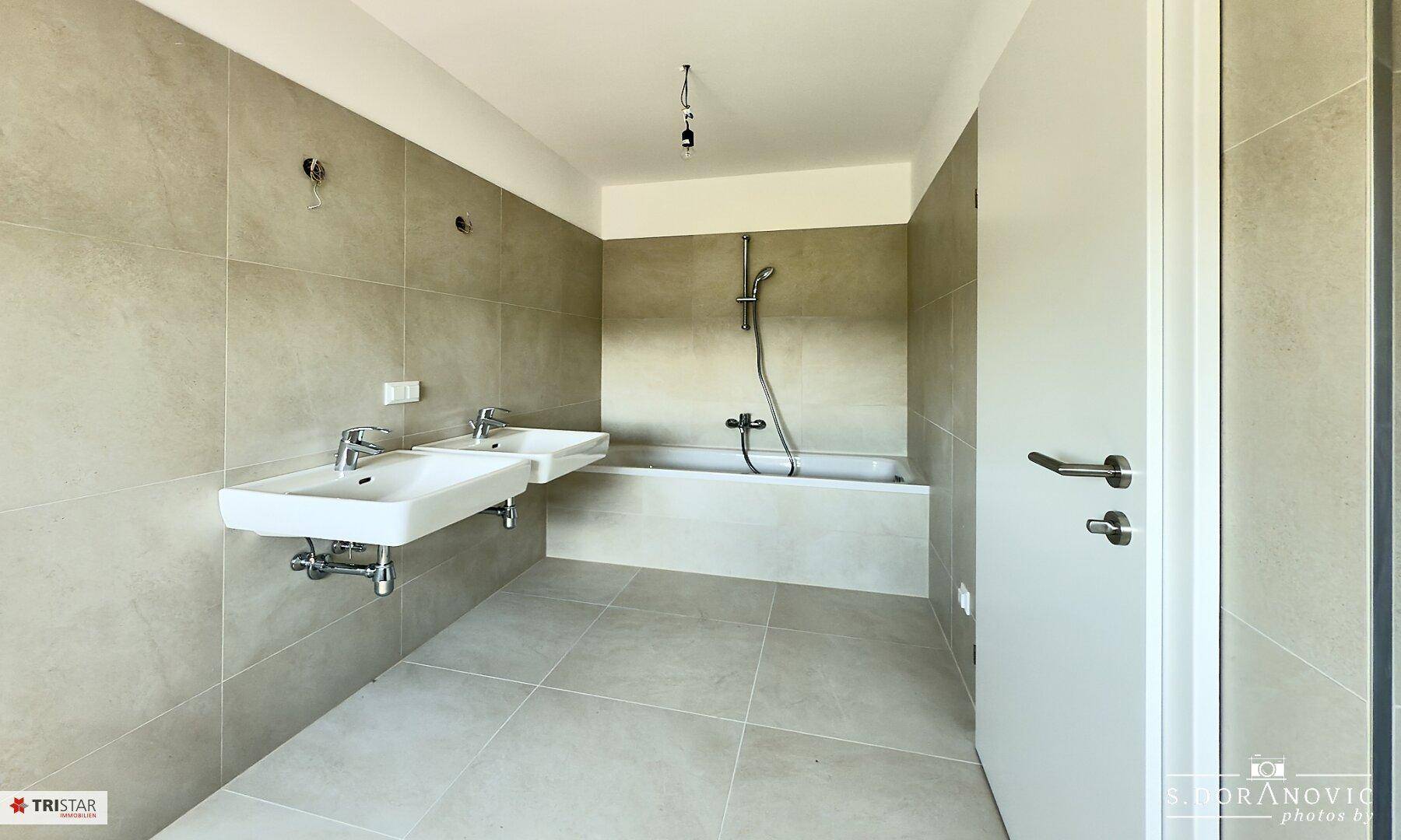 Modernes Badezimmer mit zwei Waschbecken, Badewanne und hellen Fliesen.