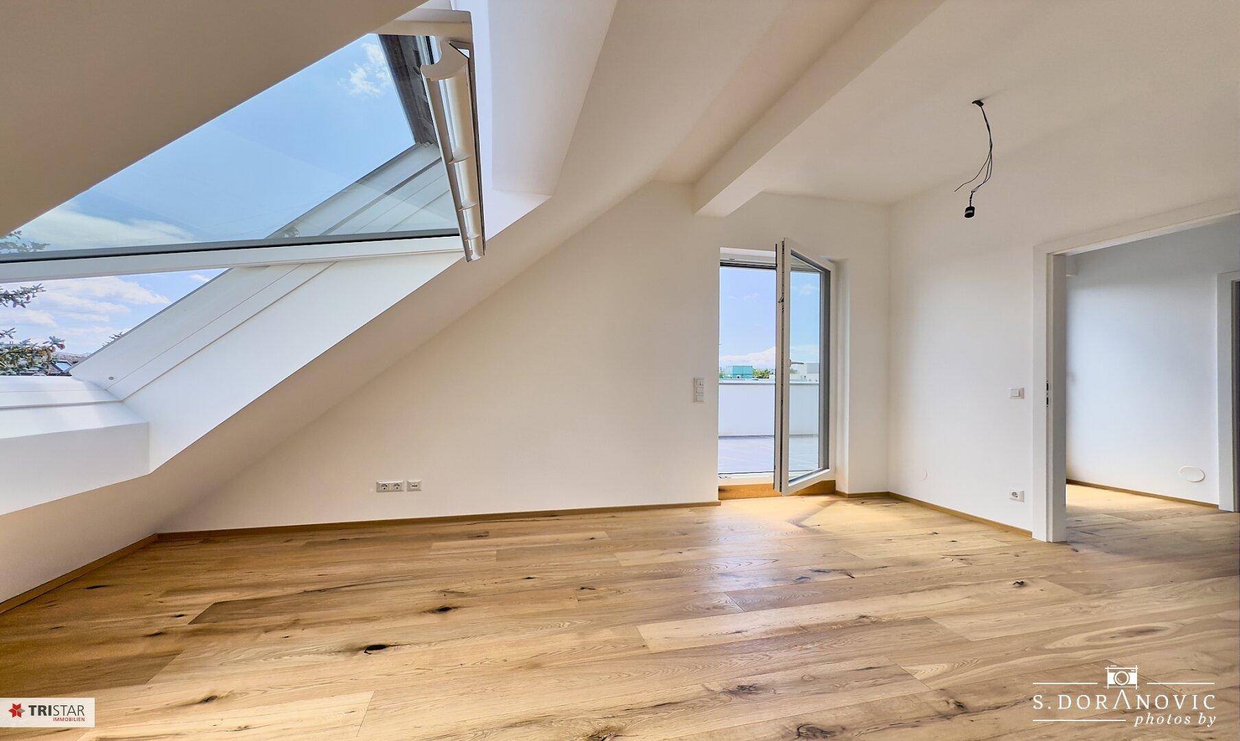 Geräumiges Zimmer mit Holzboden, großem Dachfenster und Zugang zu einem Außenbereich.