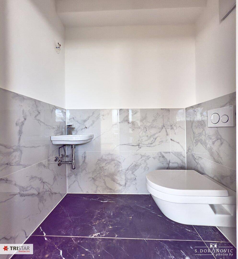 Modernes Gäste-WC mit wandhängender Toilette, kleinem Waschbecken und eleganten Marmorfliesen.