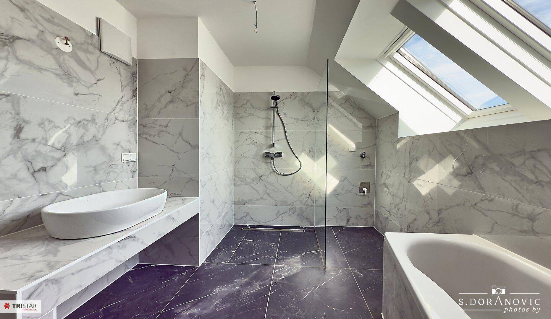 Modernes Badezimmer mit Marmorfliesen, freistehendem Waschbecken, begehbarer Dusche und Badewanne unter einem Dachfenster.