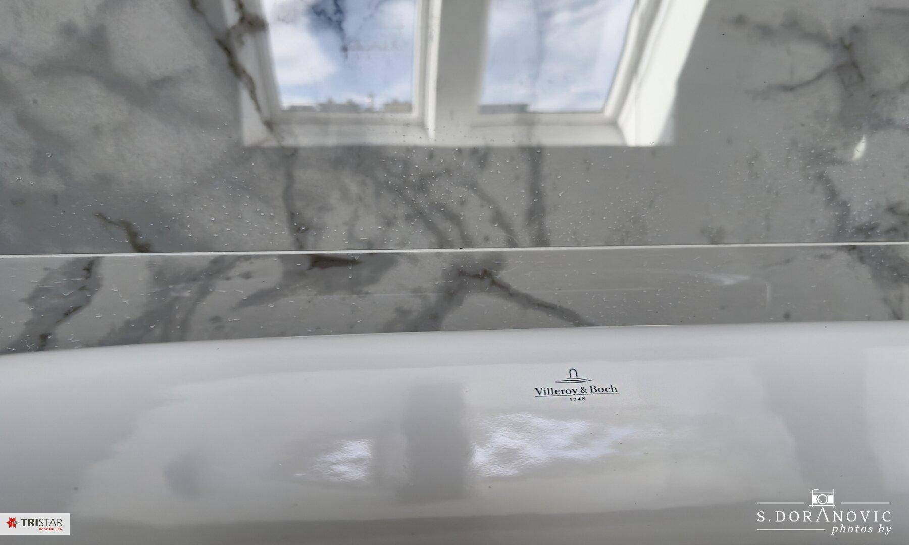 Detailaufnahme der Badewanne mit reflektierendem Dachfenster und dezentem Markenlogo.