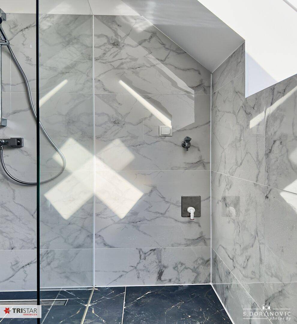 Detailansicht der begehbaren Dusche mit Marmorfliesen und modernen Armaturen, beleuchtet von Tageslicht.