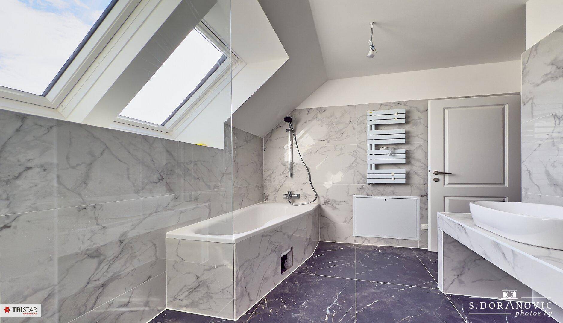 Helles Badezimmer mit Badewanne, Dusche, modernem Waschbecken und beheiztem Handtuchhalter.