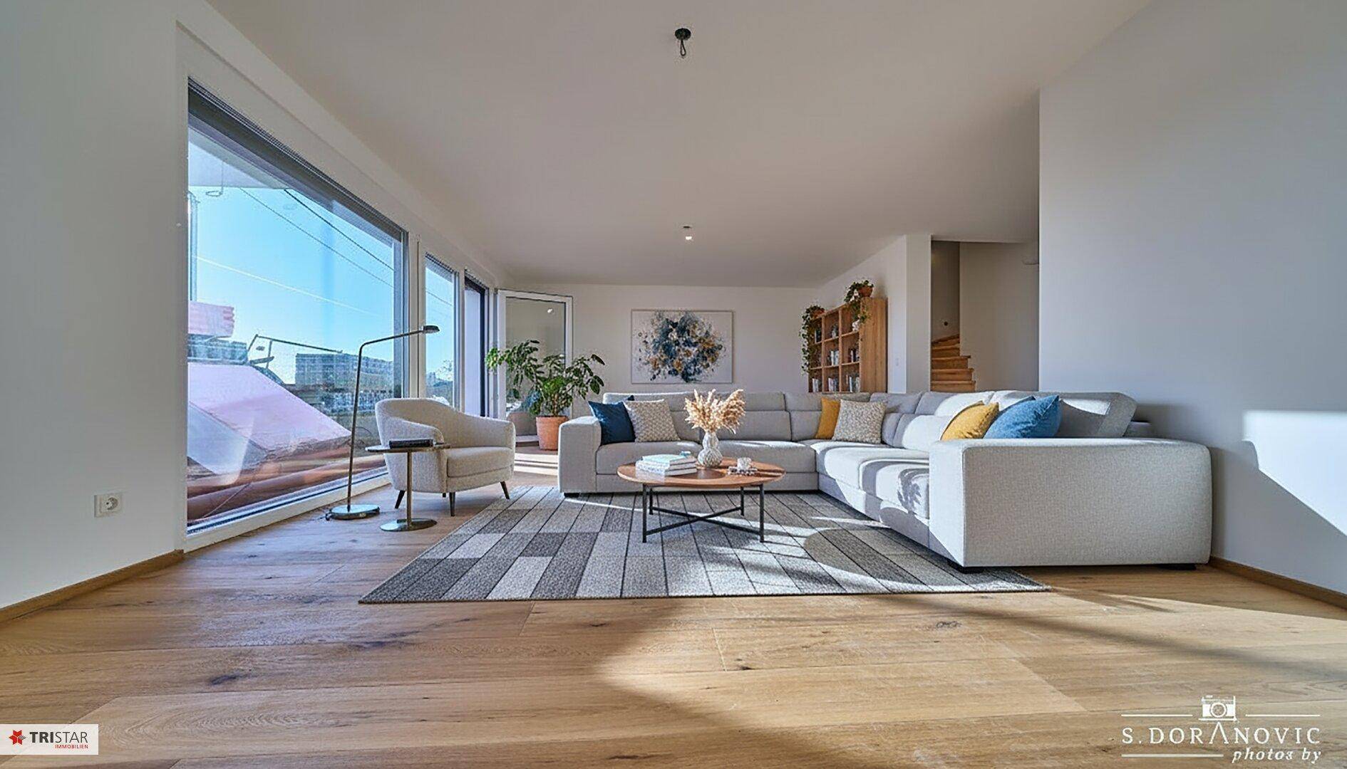 Gemütliches Wohnzimmer mit großem Sofa, Holzboden und bodentiefen Fenstern für viel Licht.