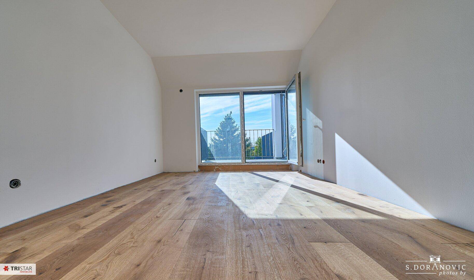 Geräumiger, leerer Raum mit neuem Holzboden und großen Fenstern, die einen weiten Ausblick bieten.