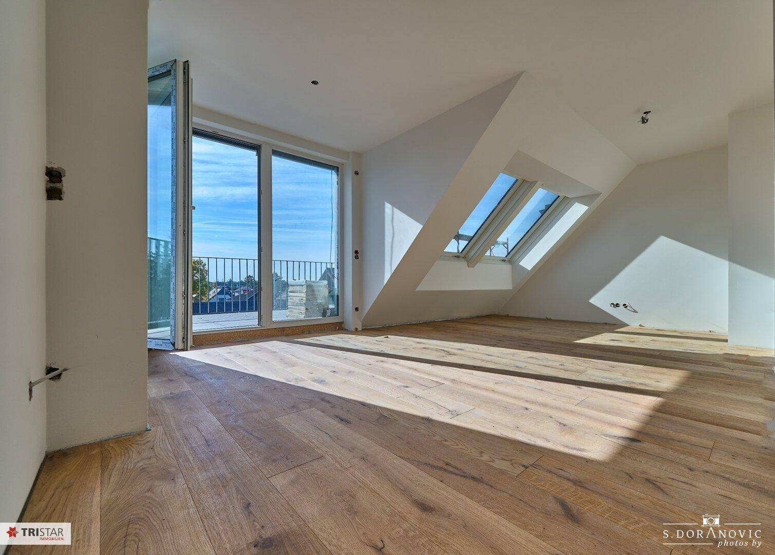 Heller Dachgeschossraum mit Holzboden, großen Fenstern und Dachfenstern für viel Tageslicht.