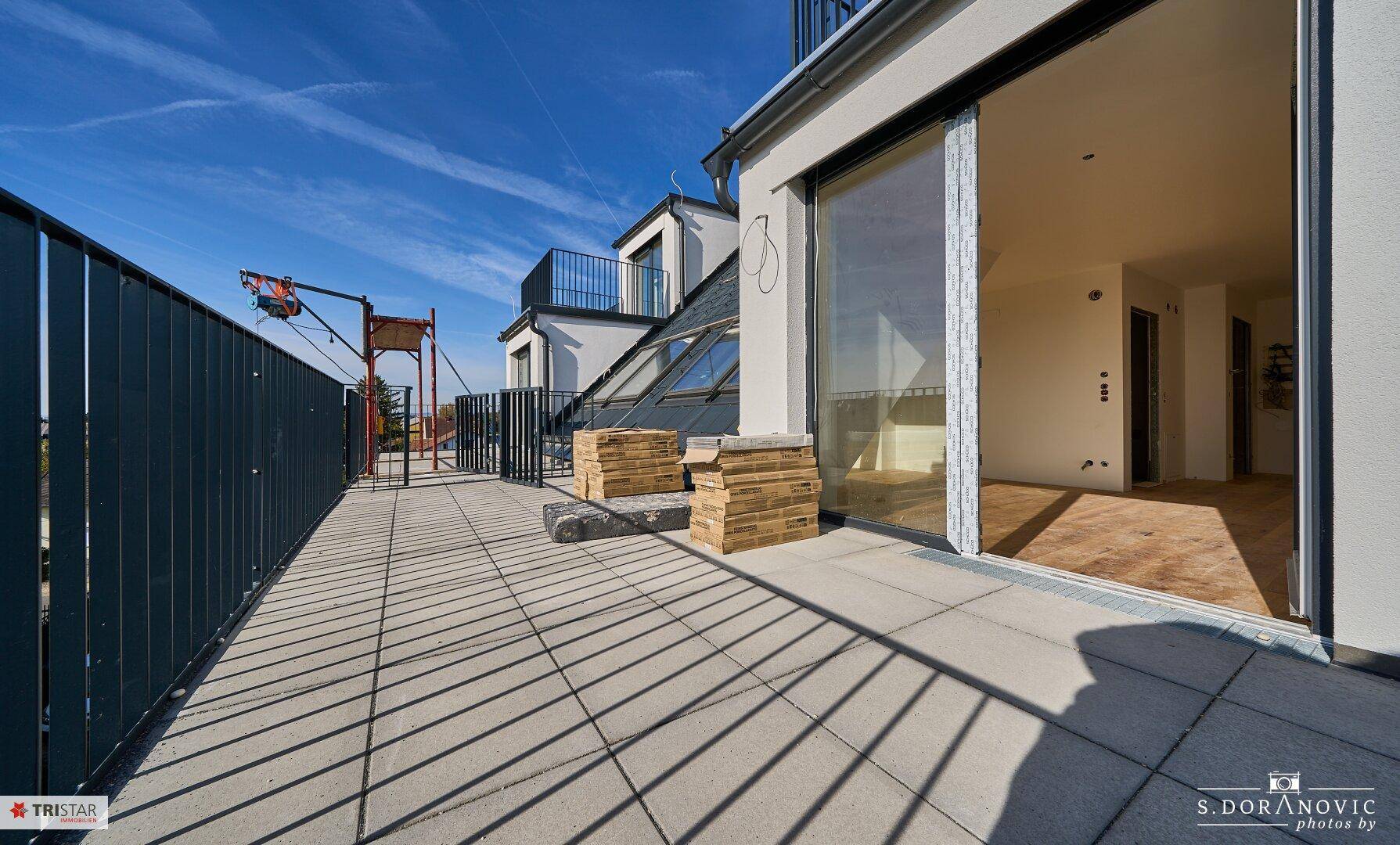 Weitläufige Dachterrasse mit Zugang zu einem hellen Innenraum und weitem Blick über die Umgebung.