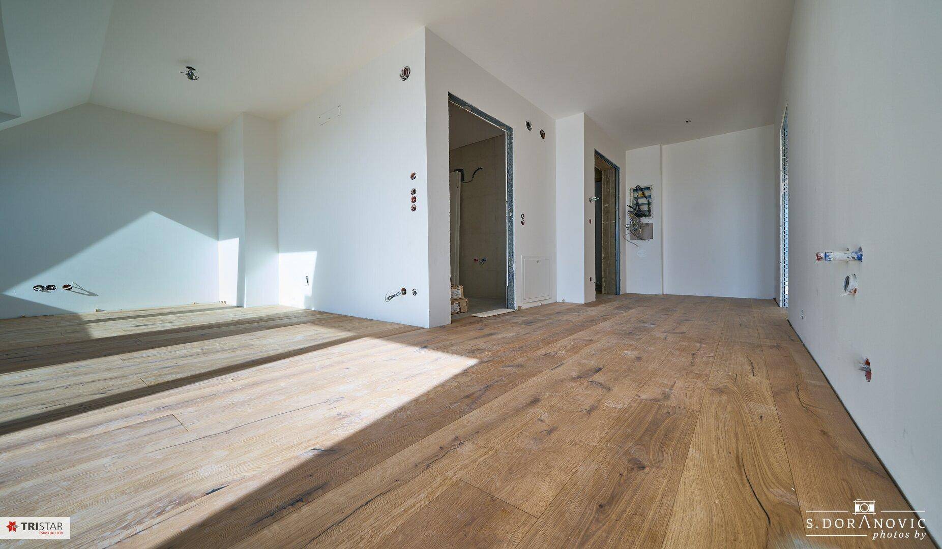 Großer, unmöblierter Raum mit Holzboden und vorbereiteten Anschlüssen, bereit für den Ausbau.