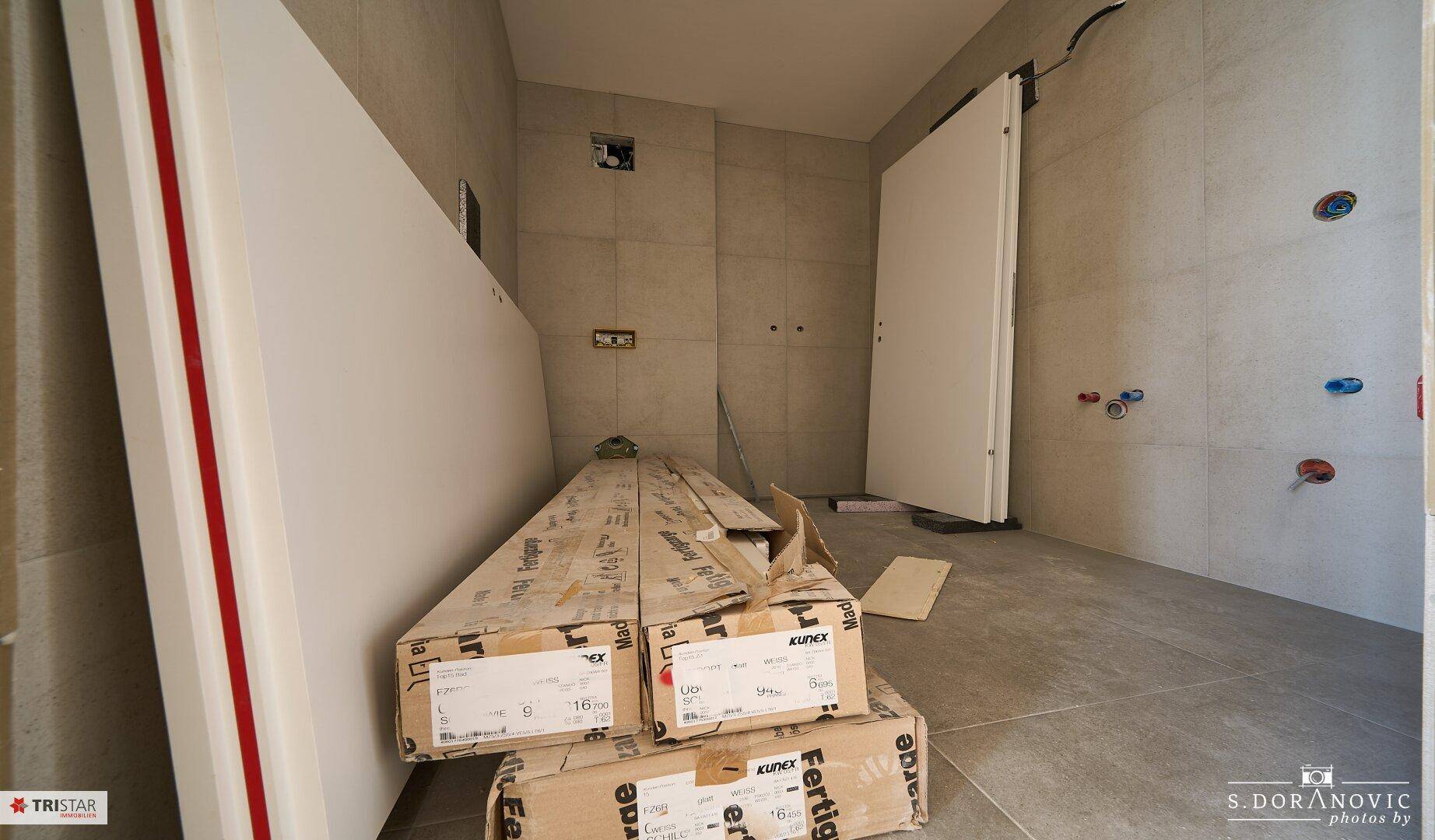 Badezimmer im Bau mit Fliesen an den Wänden und vorbereiteten Anschlüssen für Sanitärinstallationen.
