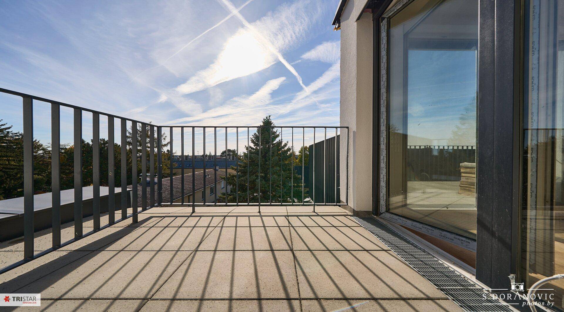 Sonniger Balkon mit Fliesenboden und Metallgeländer, bietet einen weiten Blick in die Ferne.