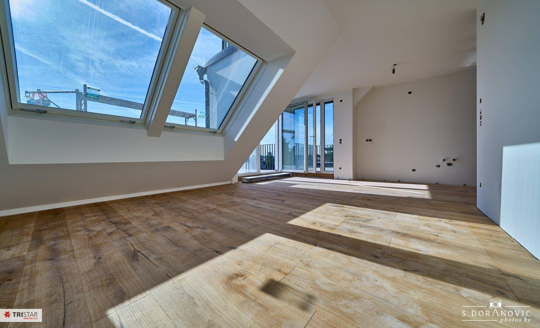Lichtdurchfluteter Raum im Dachgeschoss mit Holzboden und großen Dachfenstern.