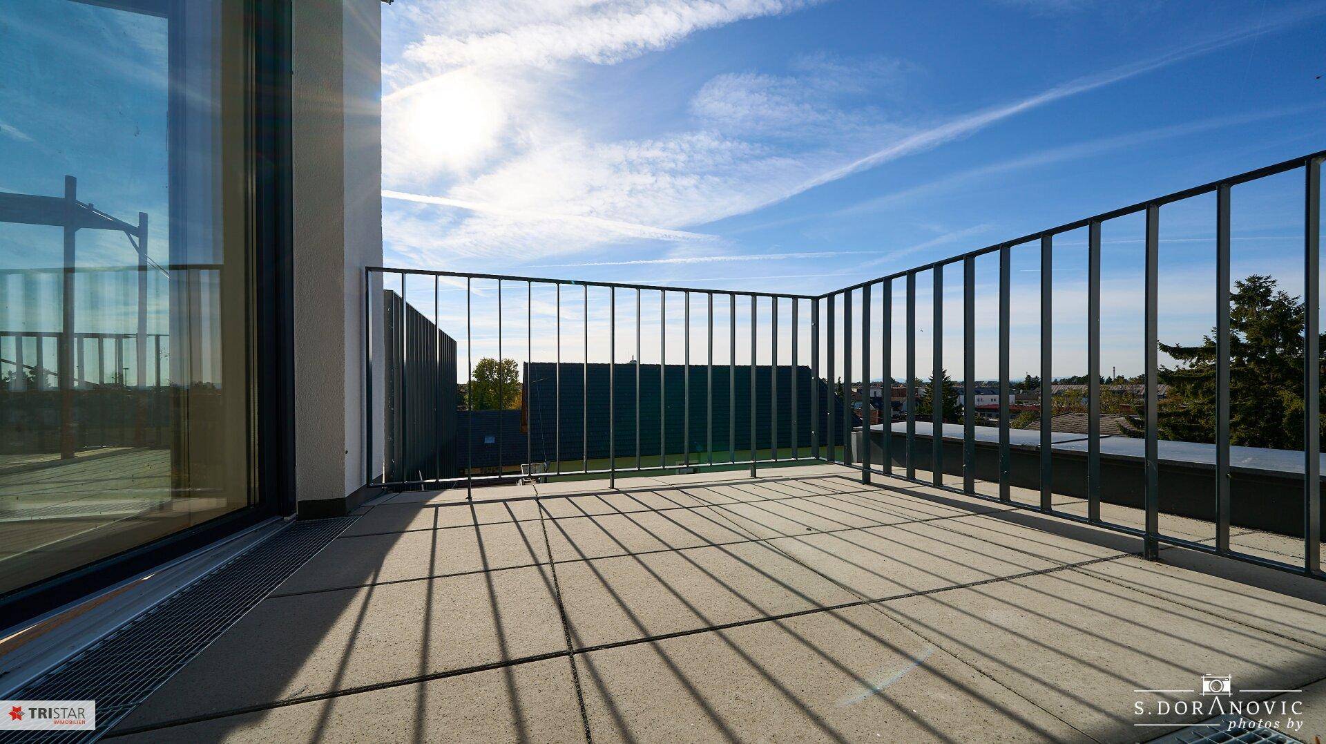 Sonniger Balkon mit Fliesenboden und Metallgeländer, bietet einen klaren Blick in die Ferne.