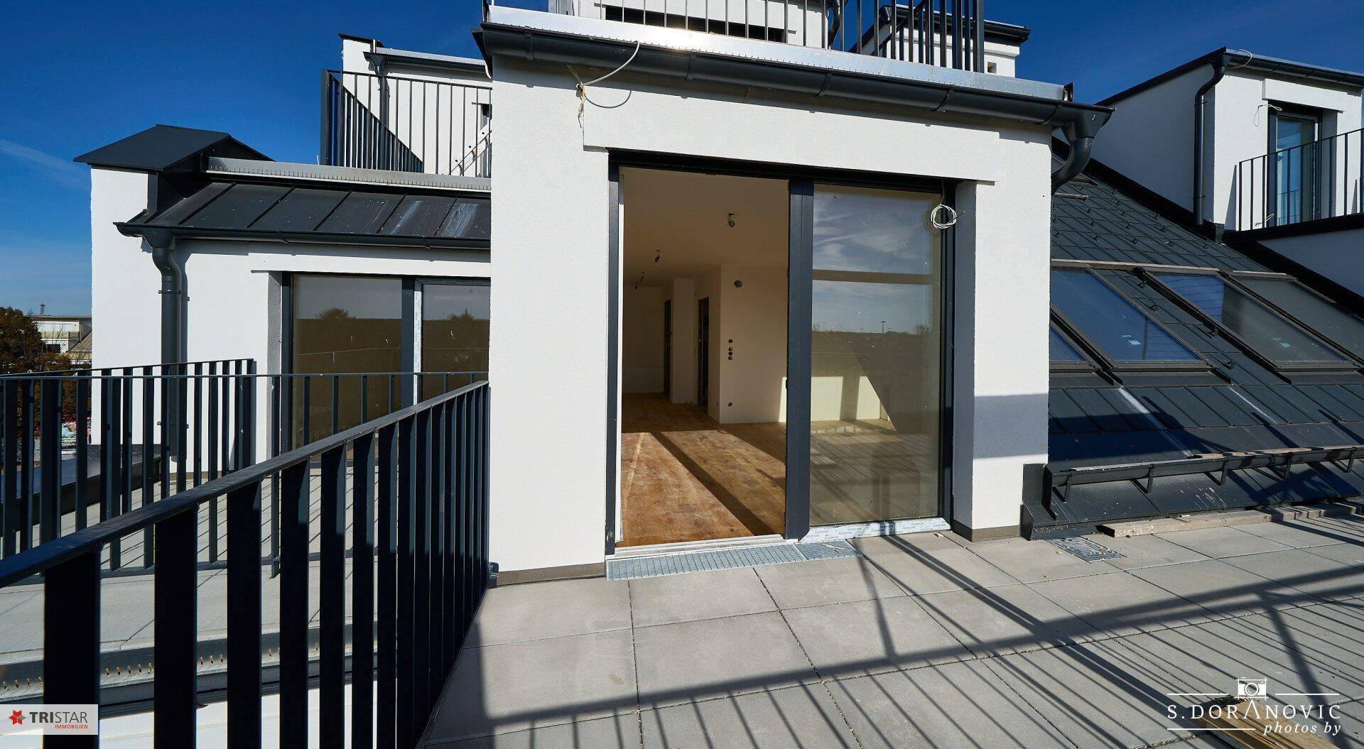 Dachterrasse mit Schiebetürzugang zu einem hellen Innenraum und Blick auf die Umgebung.