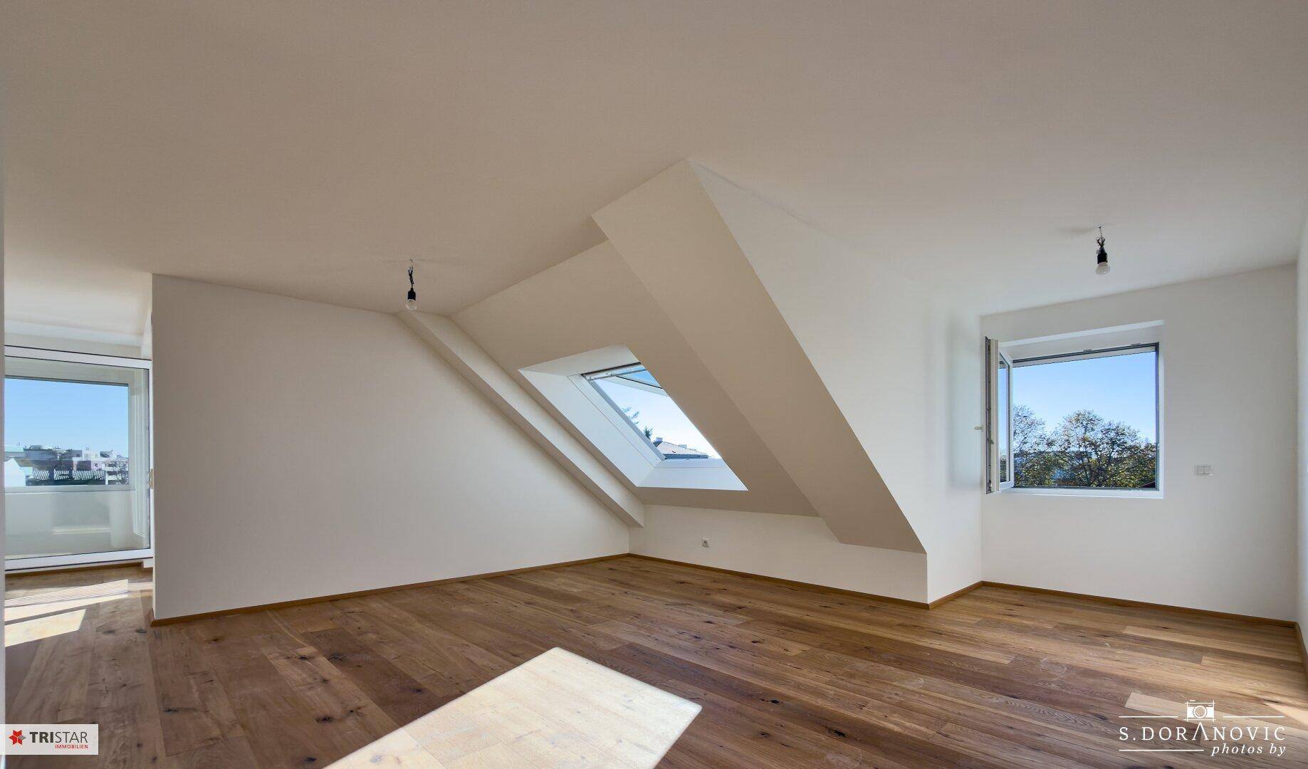 Heller, unmöblierter Wohnbereich mit Holzboden, Dachfenster und einem weiteren Fenster.