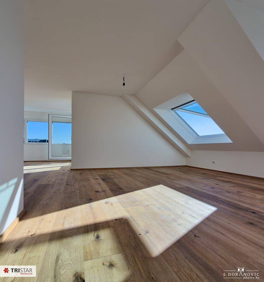 Heller, unmöblierter Wohnbereich mit Holzboden, Dachfenster und viel natürlichem Licht.