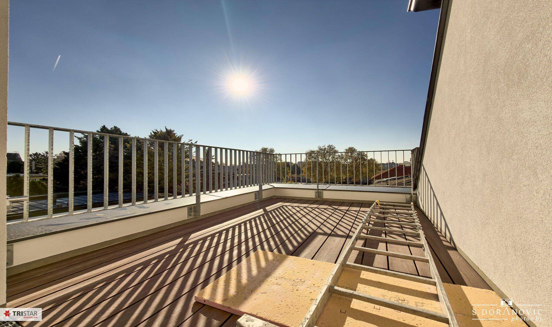 Geräumige Dachterrasse mit Holzboden und Metallgeländer unter strahlend blauem Himmel.