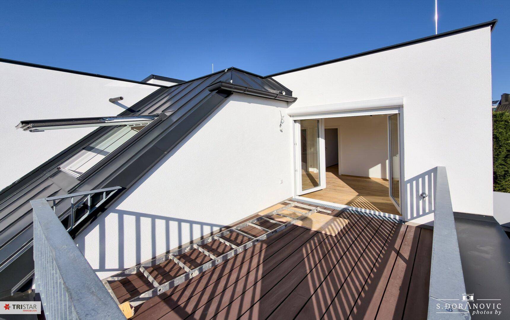 Sonnige Dachterrasse mit Holzboden und Blick auf die Umgebung, ideal für Entspannung.