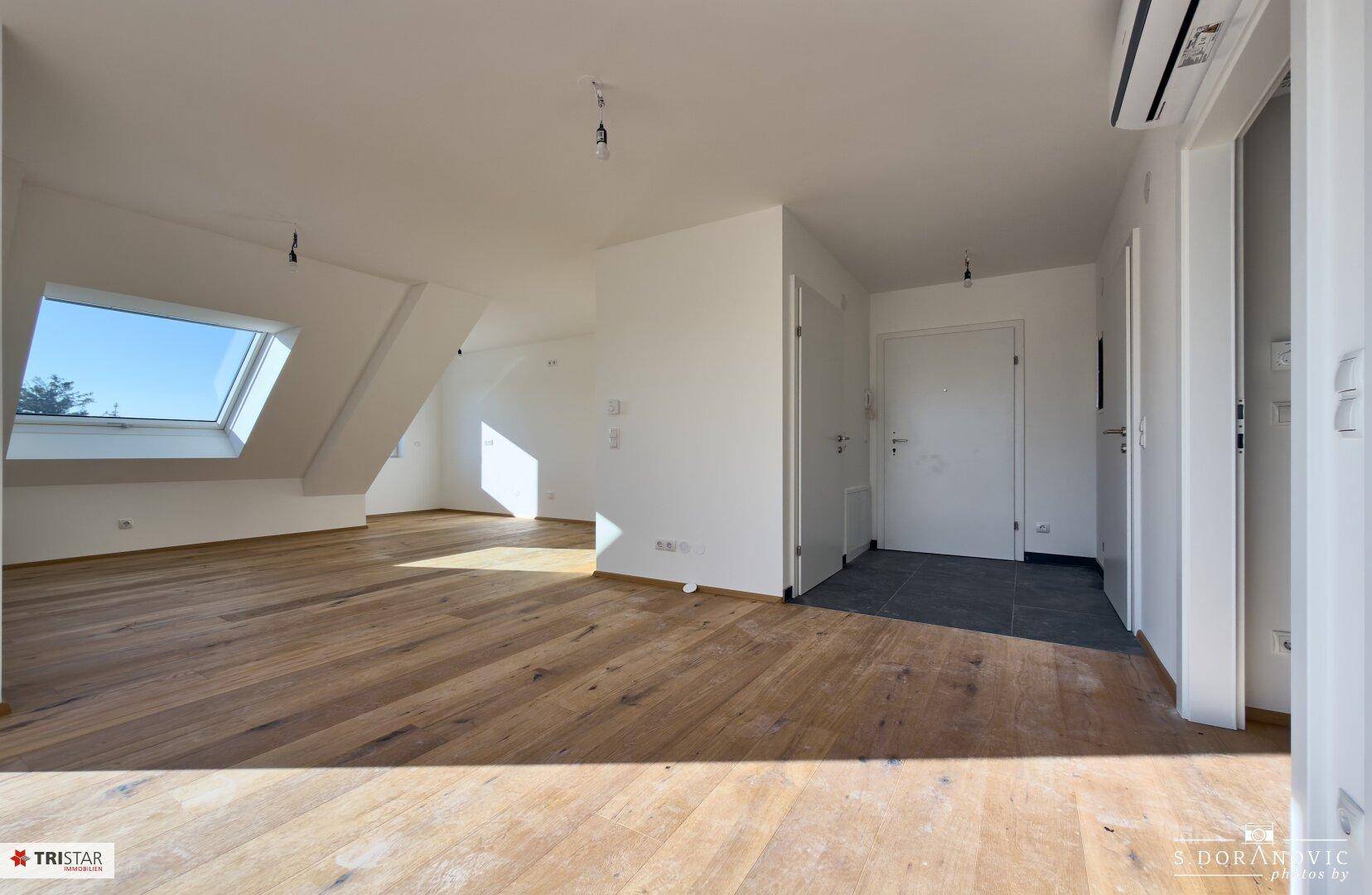 Heller, unmöblierter Wohnbereich mit Holzboden, Dachfenster und Zugang zum Flur.