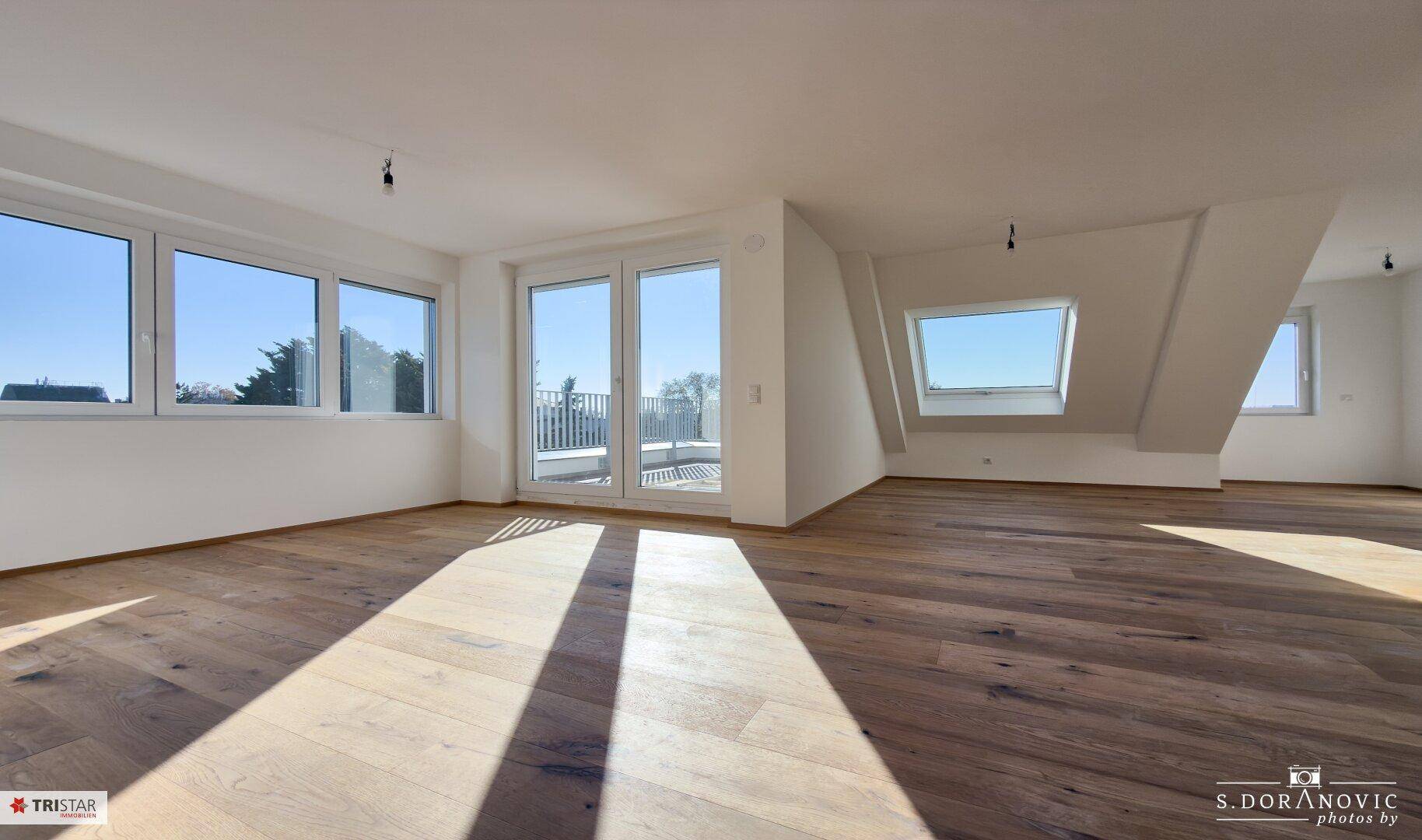 Geräumiger, unmöblierter Wohnbereich mit Holzboden, großen Fenstern und Dachfenster.