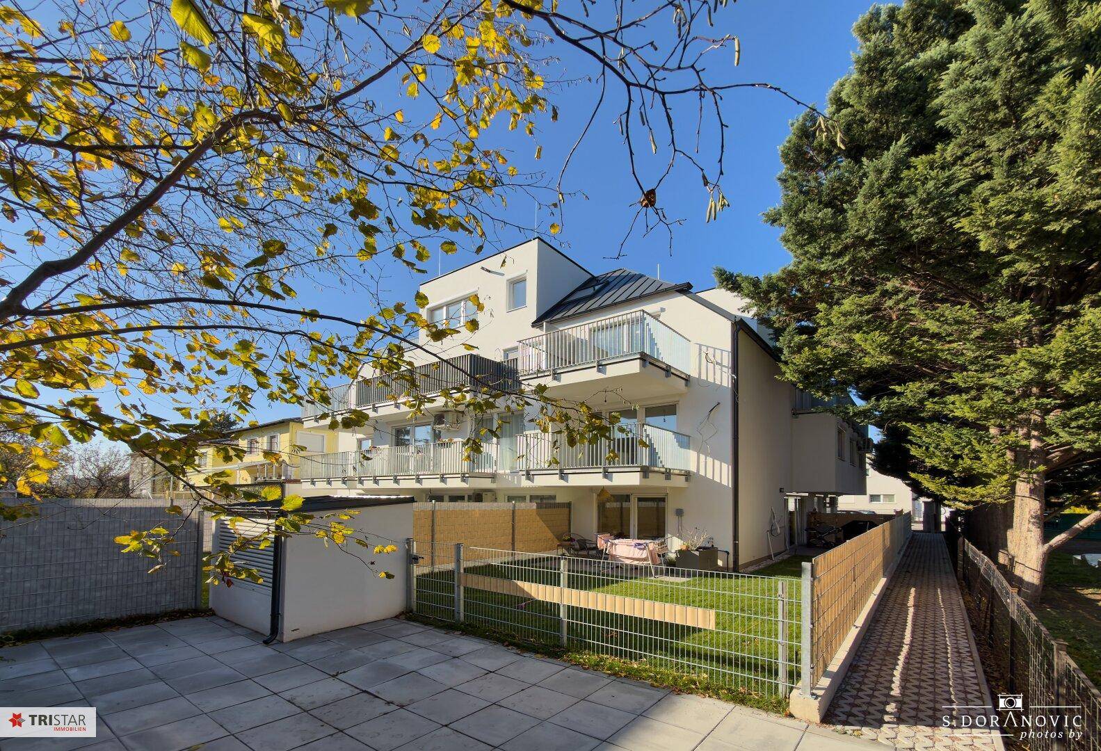 Modernes Mehrfamilienhaus mit Balkonen und gepflegter Außenanlage unter blauem Himmel.