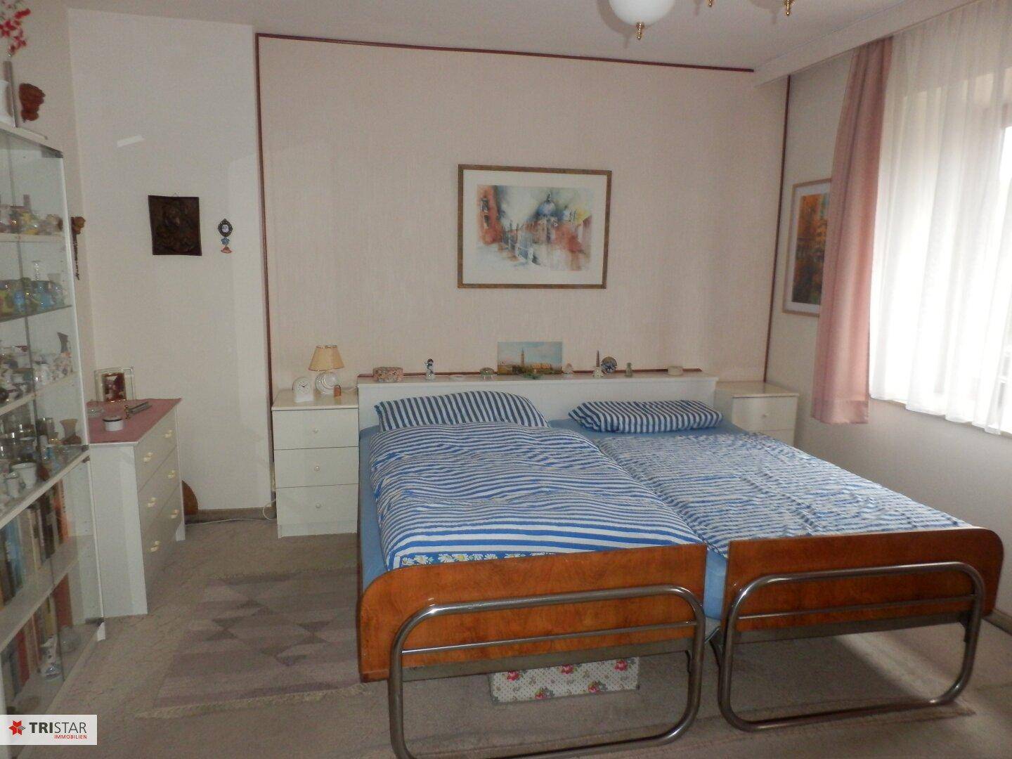 Schlafzimmer mit zwei Einzelbetten, Teppichboden und Fenster mit Vorhängen.
