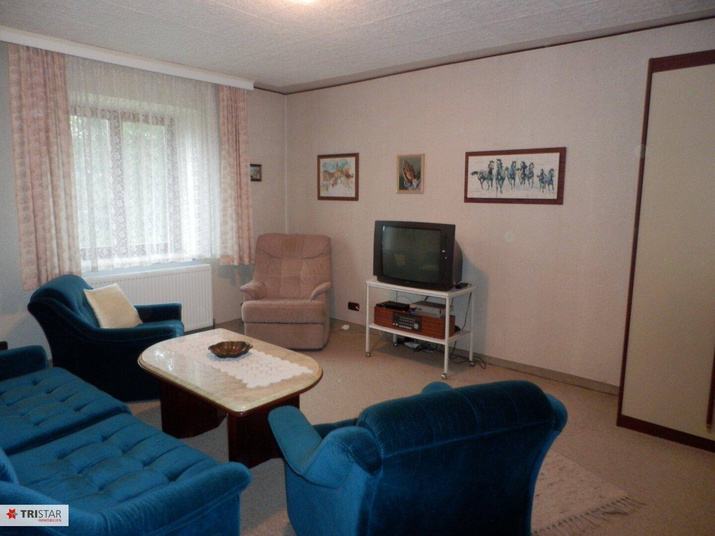 Wohnzimmer mit blauen Polstermöbeln, Teppichboden und großem Fenster.