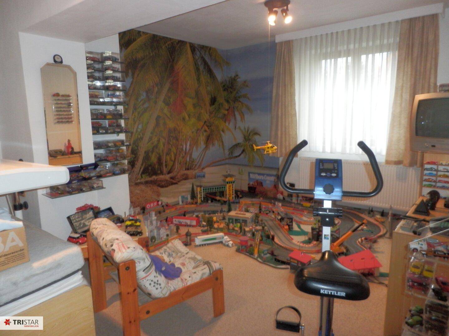 Vielseitiger Raum mit Spielzeugeisenbahn, Heimtrainer und Wandgemälde.