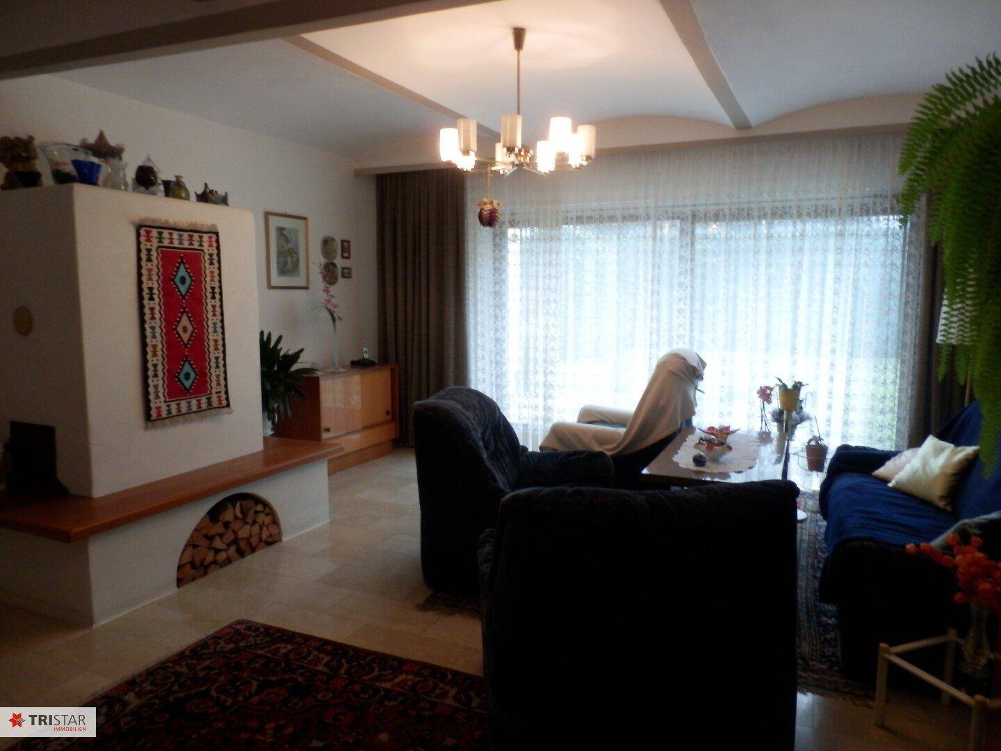 Geräumiges Wohnzimmer mit Kamin, Fliesenboden und großen Fenstern.