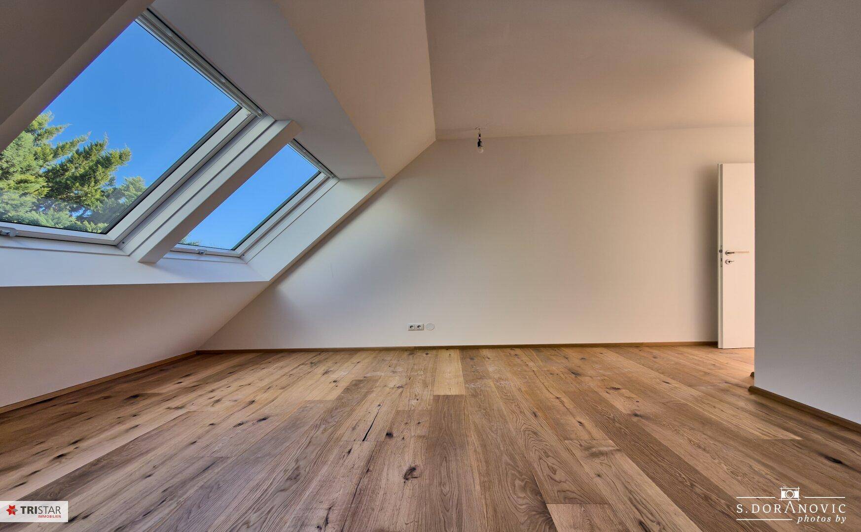 Helles Zimmer mit Holzboden und zwei großen Dachfenstern, die viel Licht spenden.