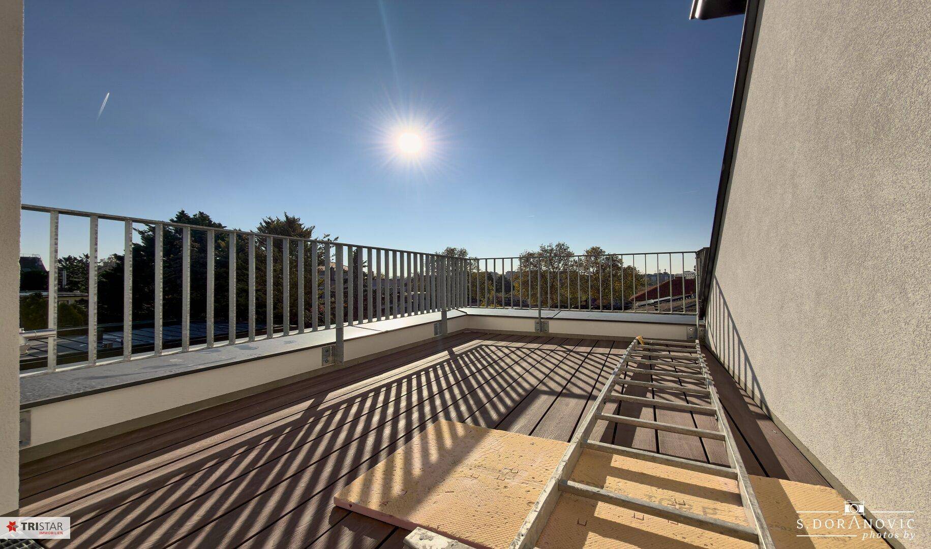 Sonnige Dachterrasse mit Holzdielenboden und Metallgeländer, ideal zum Entspannen im Freien.