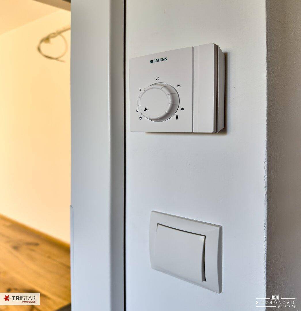 Ein Siemens-Thermostat und ein Lichtschalter sind an einer weißen Wand montiert.