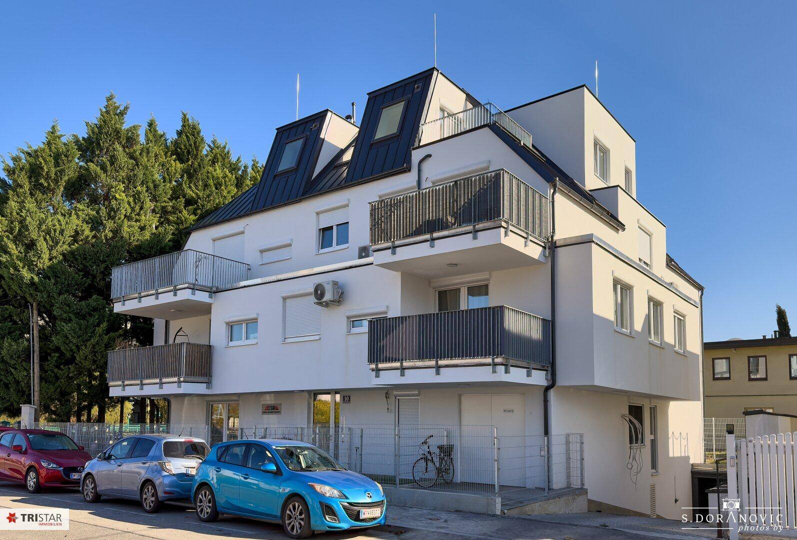 Seitenansicht des modernen Apartmentgebäudes von der Straße mit Balkonen und geparkten Autos.