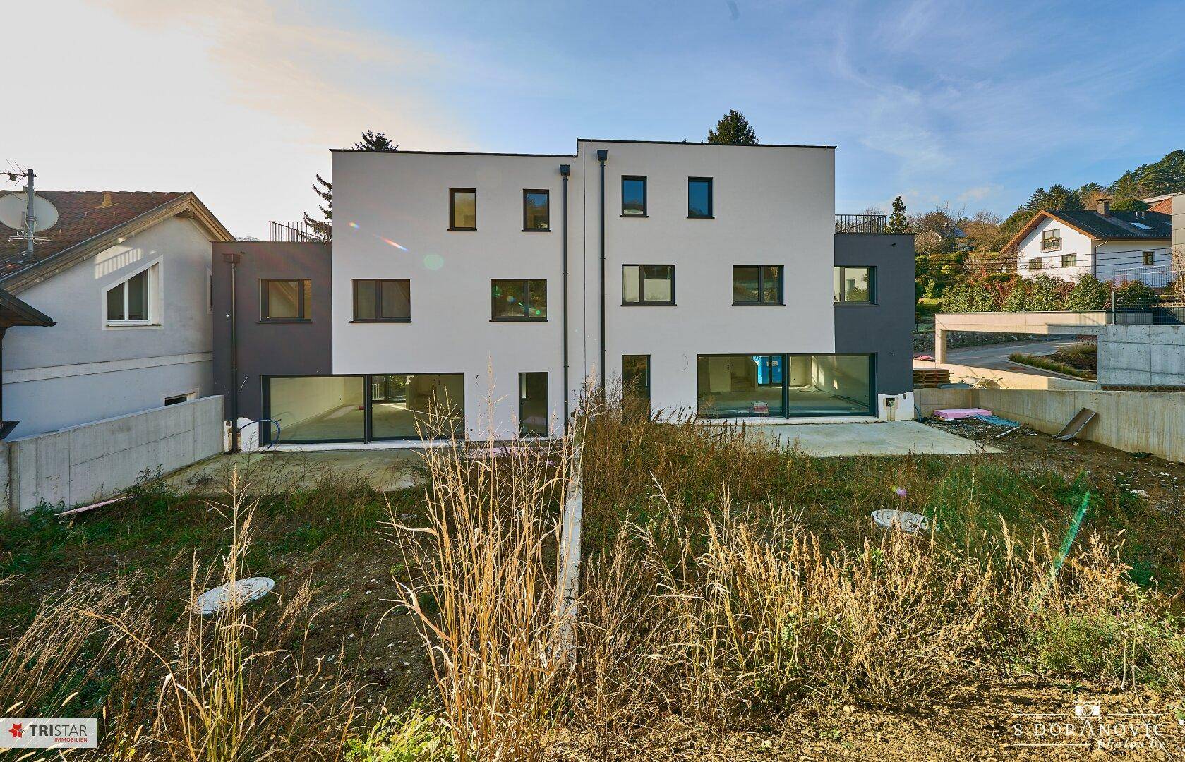 Rückansicht zweier moderner Reihenhäuser mit großen Fensterfronten und einem noch ungestalteten Gartenbereich.