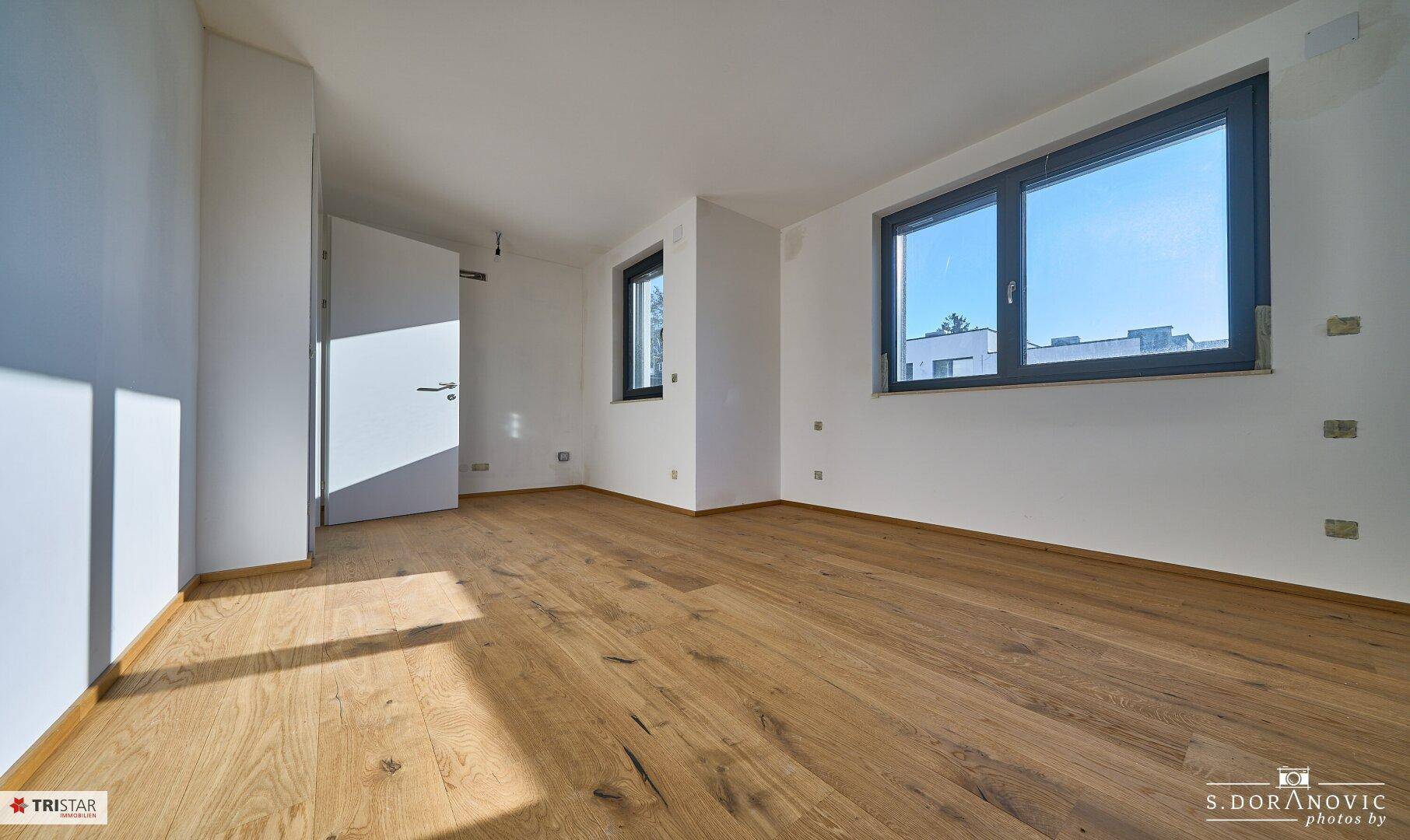 Helles Zimmer mit Holzboden und Fenstern, die viel Tageslicht hereinlassen, ideal für ein Schlafzimmer.