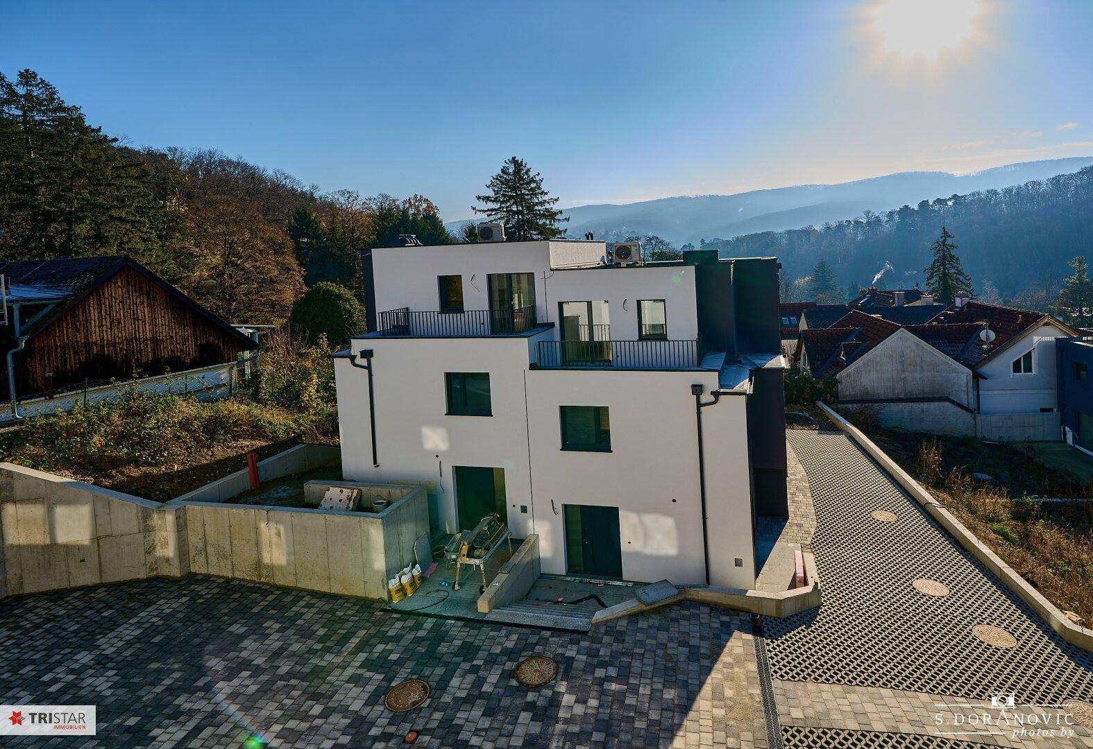 Moderne Wohnanlage mit weißer Fassade und Balkonen, umgeben von grüner Landschaft unter blauem Himmel.